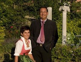 Gastgeberpaar in traditioneller Tracht lächelt in die Kamera.