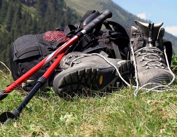 Bergschuhe, Wanderstöcke und ein Rucksack liegen auf einer Wiese.