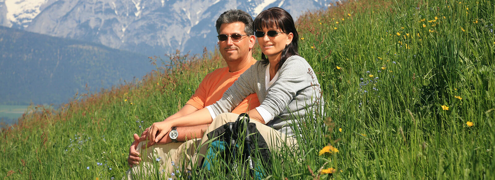 Ein Paar mit Sonnenbrillen sitzen zusammen in einer grünen Wiese.
