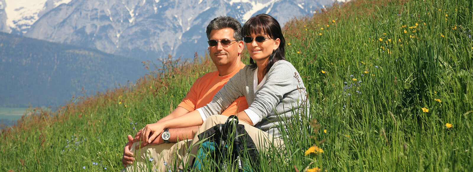 Ein Paar mit Sonnenbrillen sitzen zusammen in einer grünen Wiese.