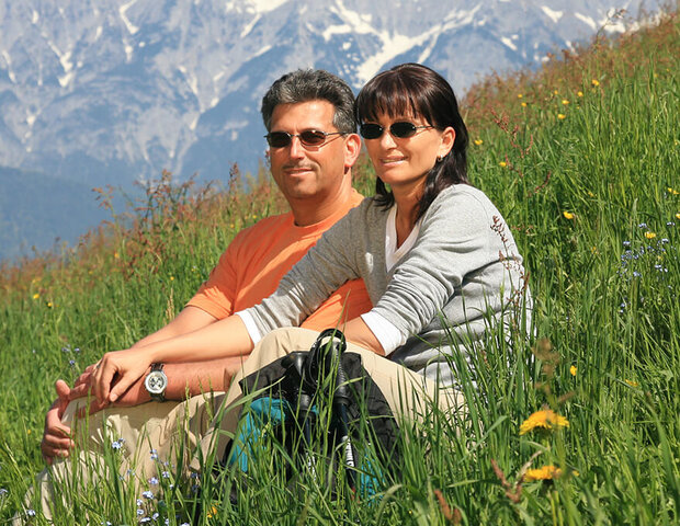 Ein Paar mit Sonnenbrillen sitzen zusammen in einer grünen Wiese.