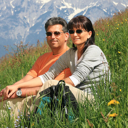Ein Paar mit Sonnenbrillen sitzen zusammen in einer grünen Wiese.