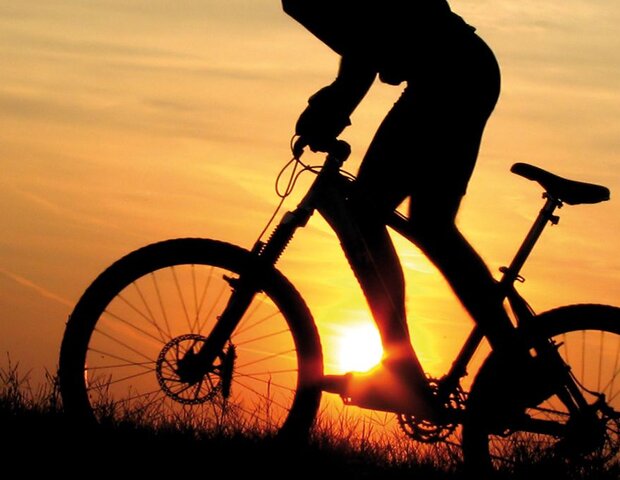 Eine Mountainbiker fährt bei Sonnenaufgang.